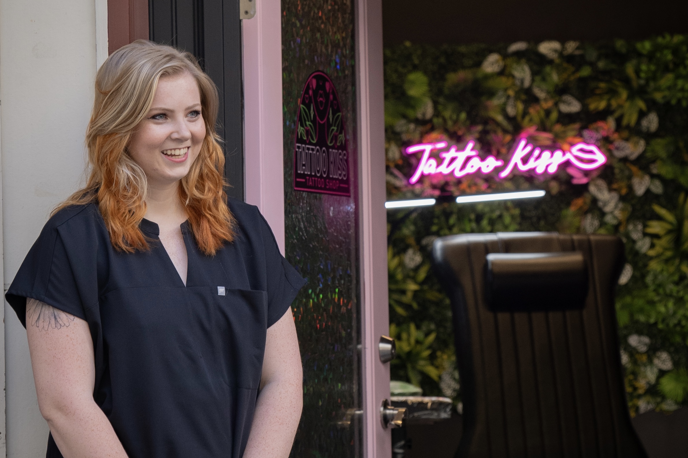 Owner and tattoo artist at Tattoo Kiss, smiling and laughing in front of the custom tattoo studio in Portland, welcoming clients with a friendly demeanor.